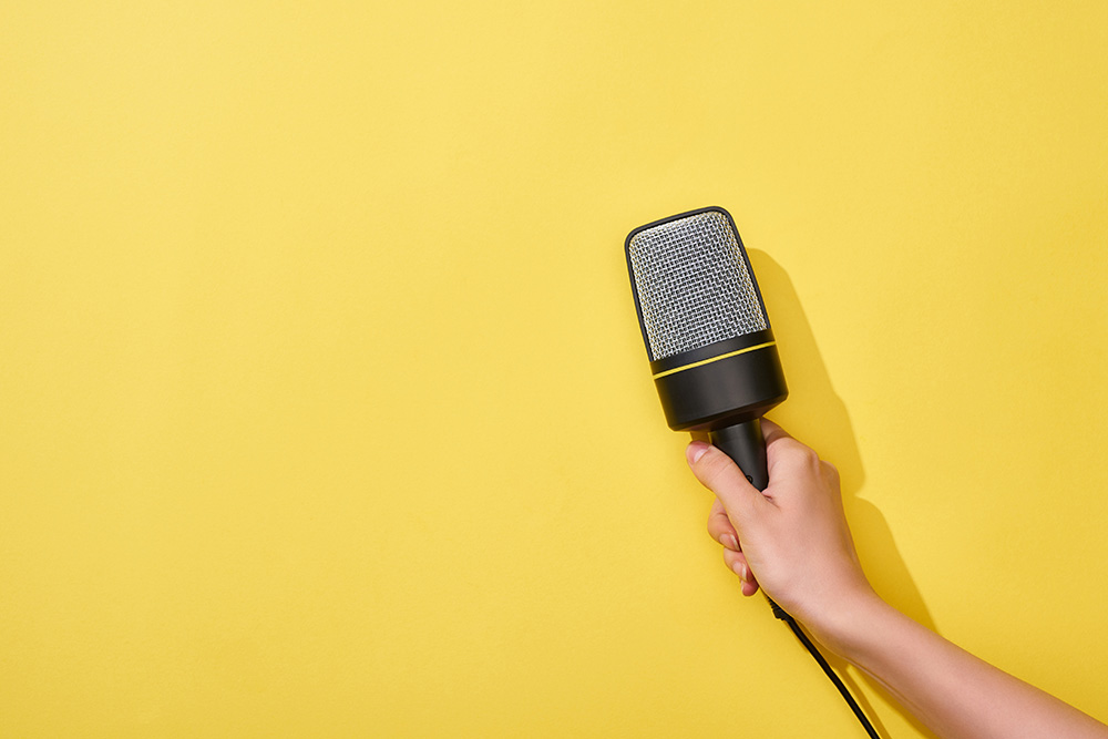 cropped view of woman holding microphone on yellow background