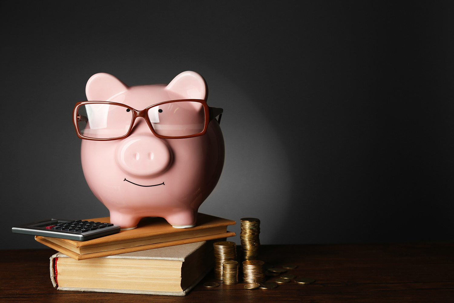 Piggy bank with glasses ,coins and books on table , gray background